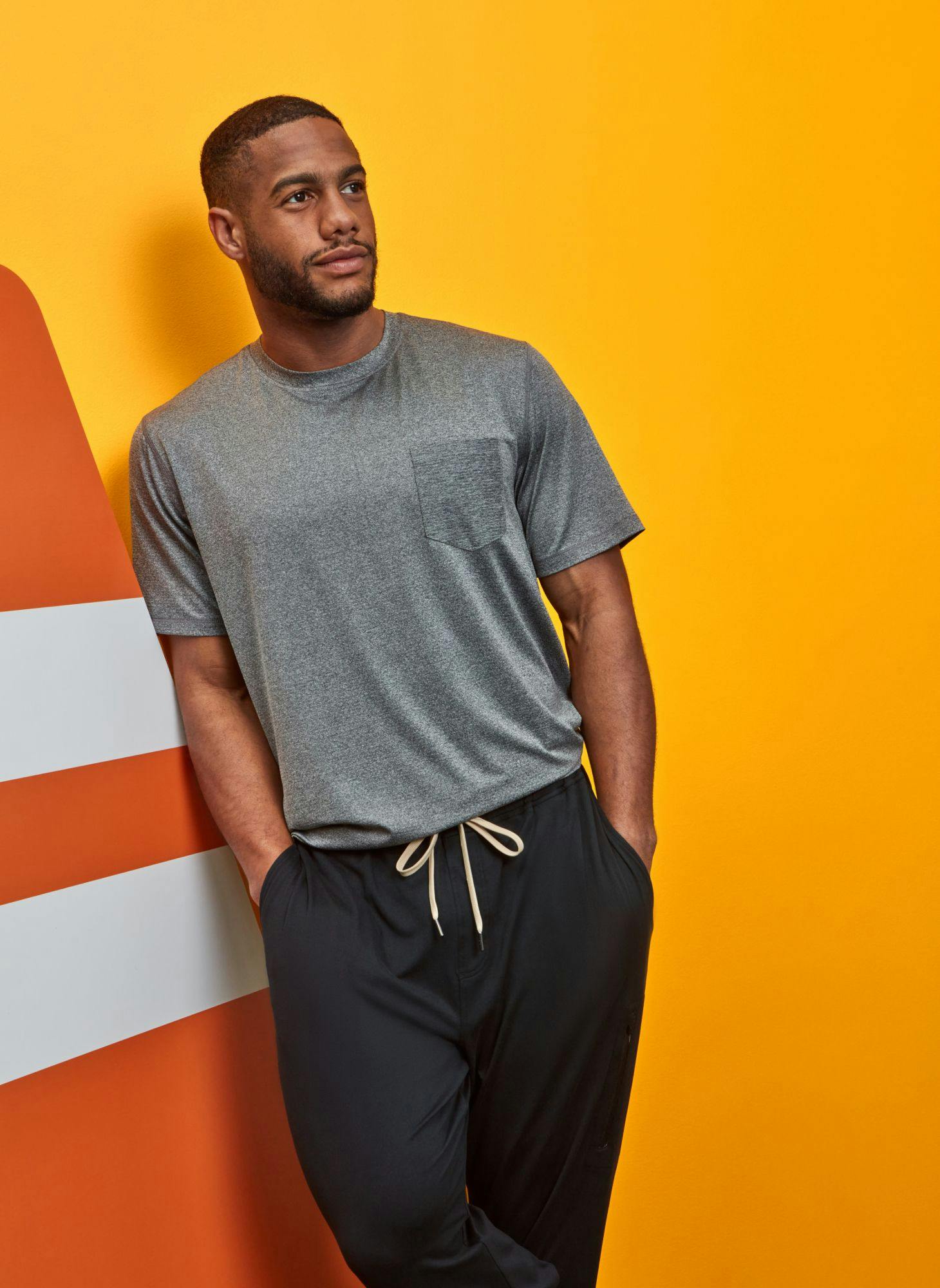 Man poses in activewear in front of a yellow and orange background