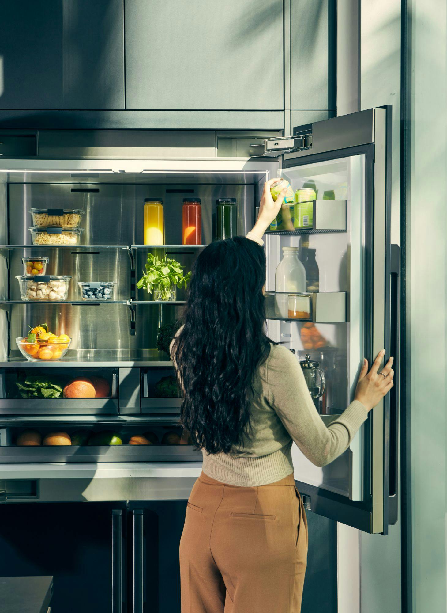 A woman grabbing beverage from an open refrigerator door