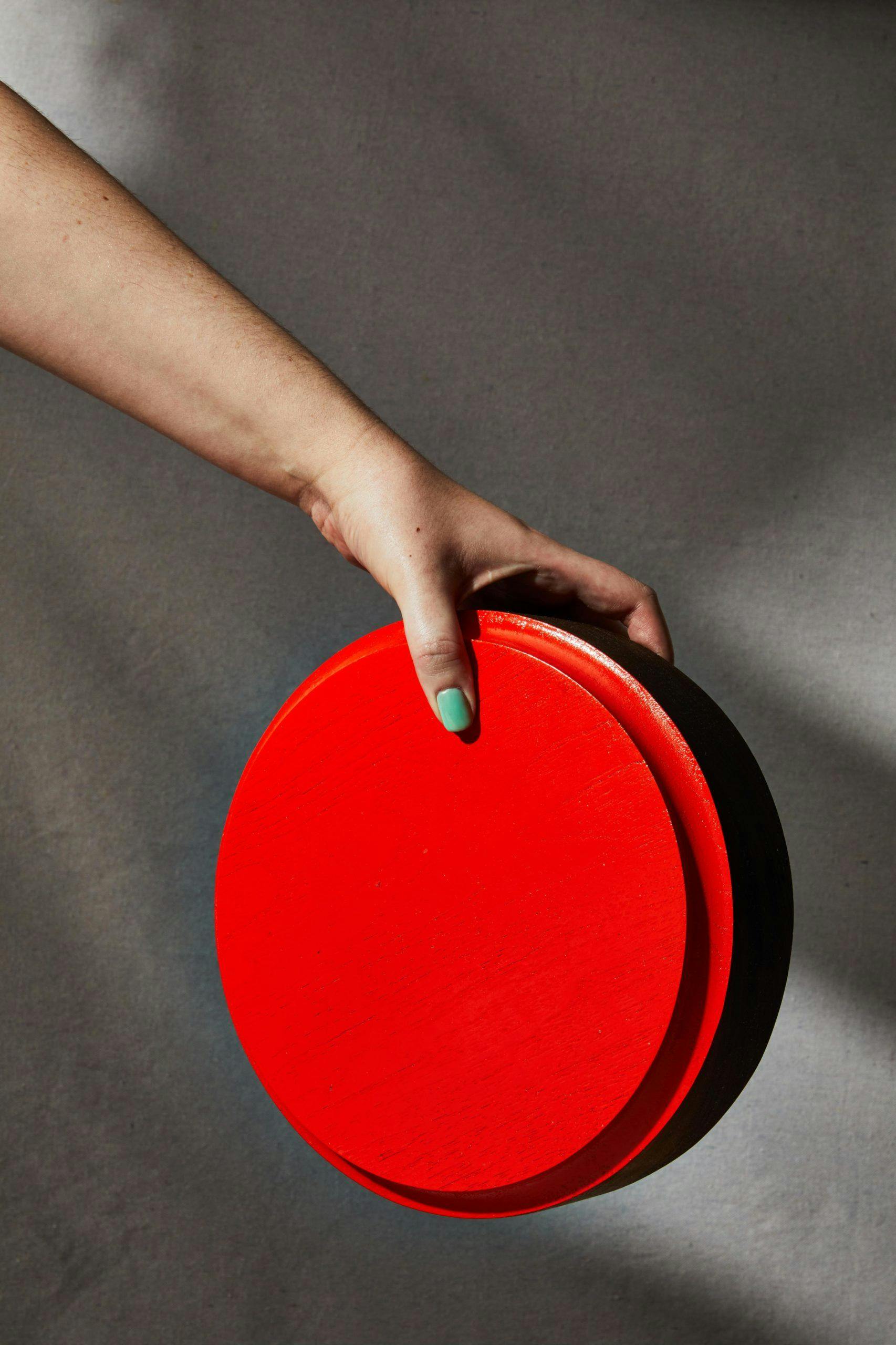 Hand holding a red plate against a gray background