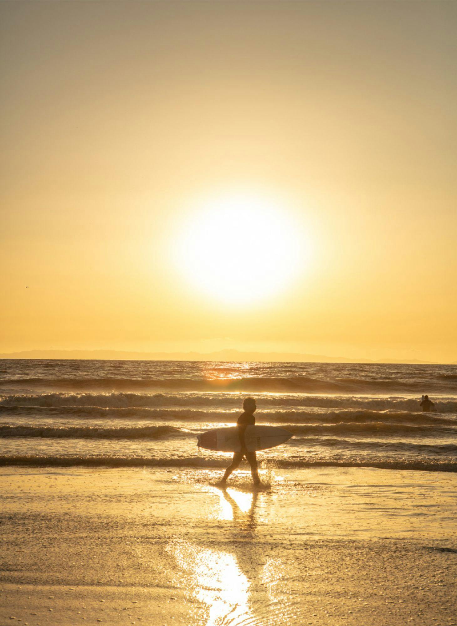 A surfer with surfboard running toward the ocean around sunset
