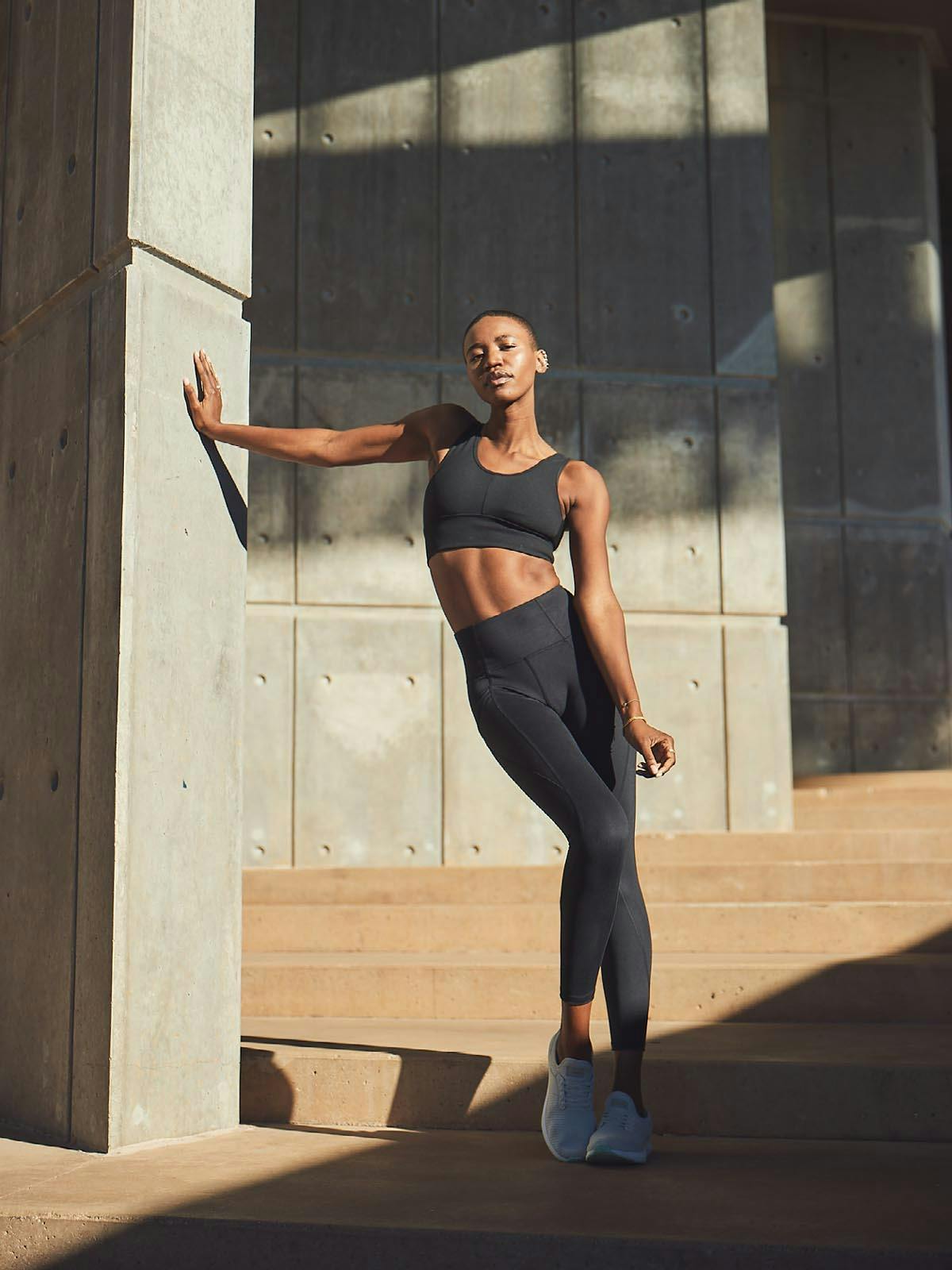 Woman Posing in a Shadowy Walkway Wearing a Black Athleisure Set